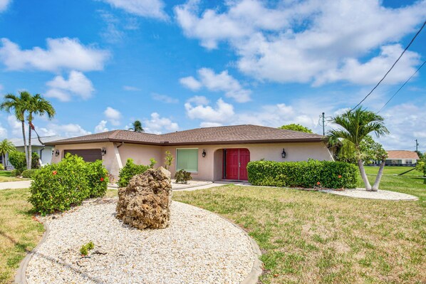 A single-story house with a red door, surrounded by a well-maintained lawn and palm trees. - Private Dock & 2 Mi to Beach! Cape Coral Getaway (Cape Coral)