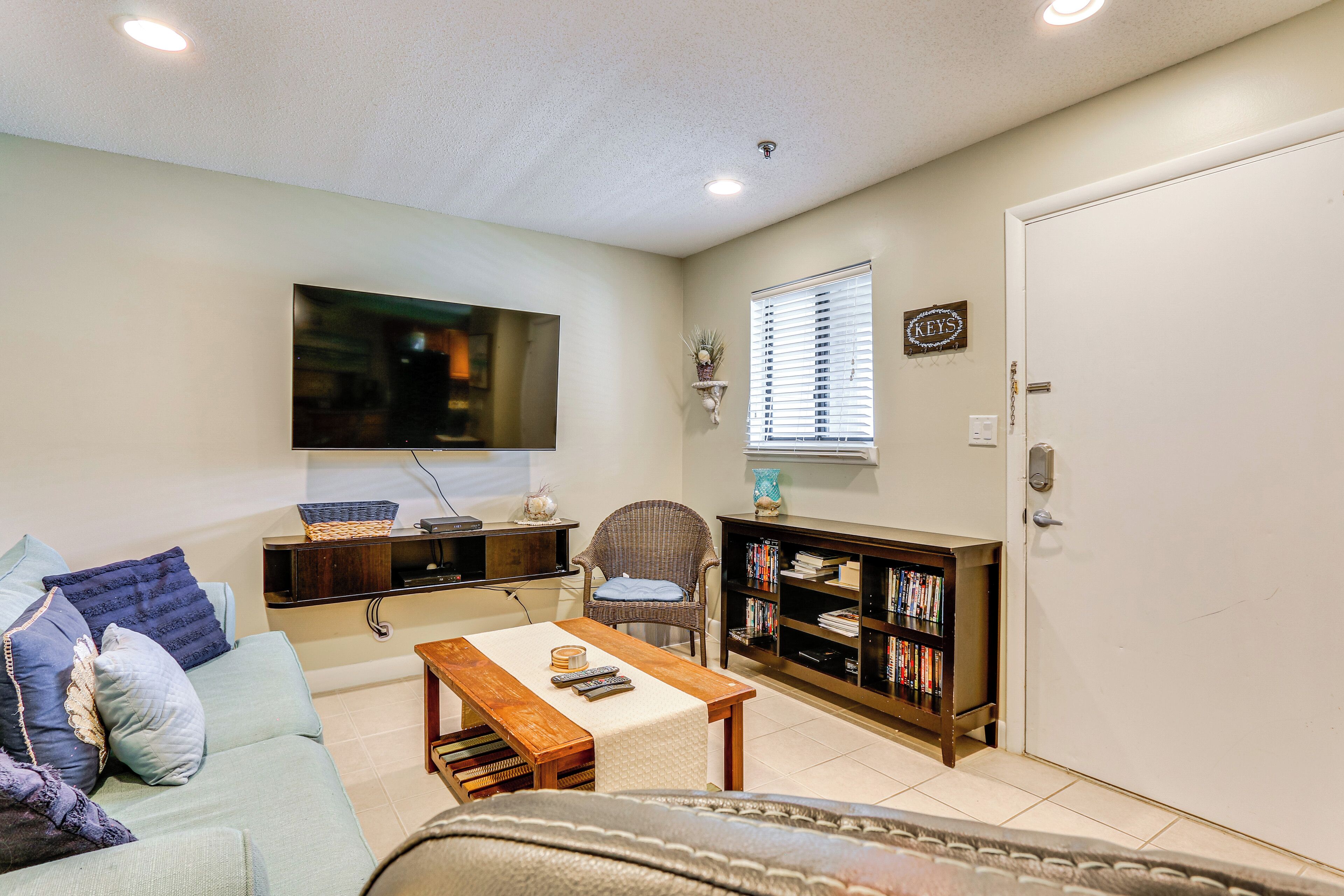 A living room with a sofa, a coffee table, a bookshelf, a television mounted on the wall, and a door with a key lock.