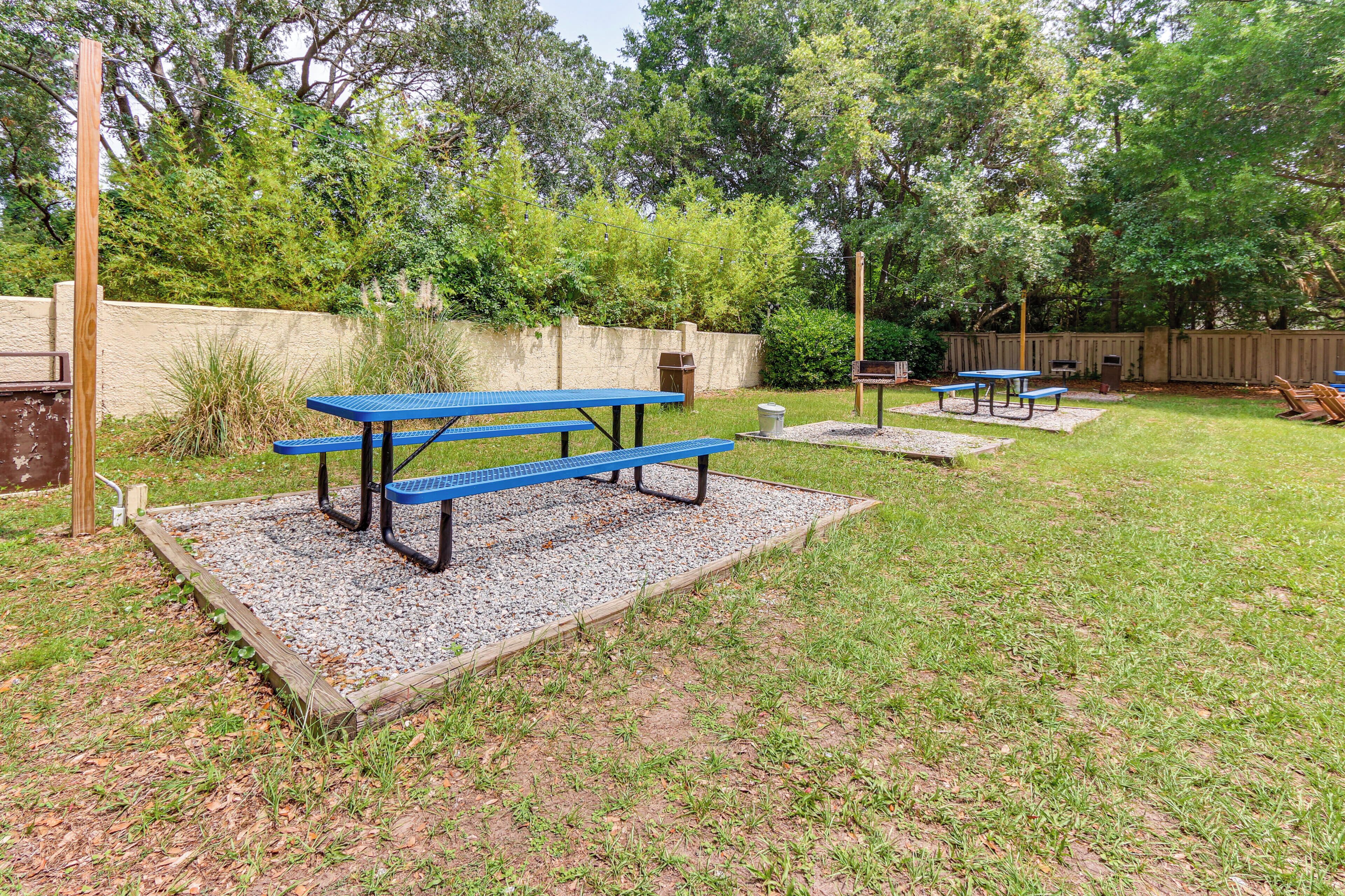 Un jardin avec des tables de pique-nique, une clôture en bois et un espace recouvert de gravier.