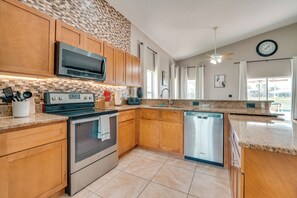 A modern kitchen with wooden cabinets, stainless steel appliances, a granite countertop, and a large window. - 11 Mi to Disney: Home w/ Game Room & Heated Pool (Davenport)