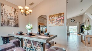 A dining area with a wooden table, leather chairs, and a chandelier. There are paintings on the walls and a kitchen in the background. - 11 Mi to Disney: Home w/ Game Room & Heated Pool (Davenport)