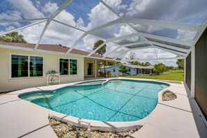 A swimming pool with a covered patio area, clear blue water, and a view of a house in the background. - Pool & Spa: Canal-front Home Near Beaches (Rotonda West)