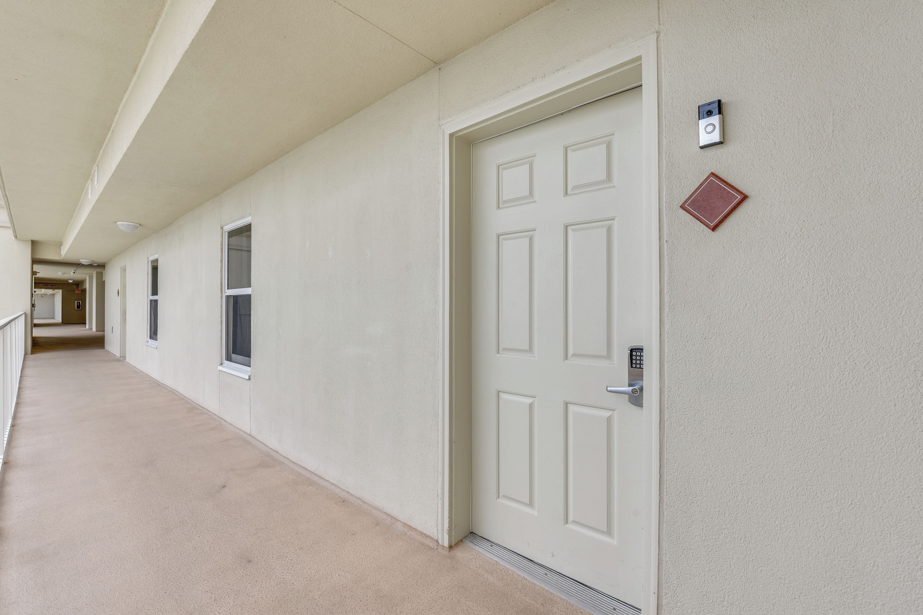 A hallway with a white door, a security camera, and a fire alarm on the wall.
