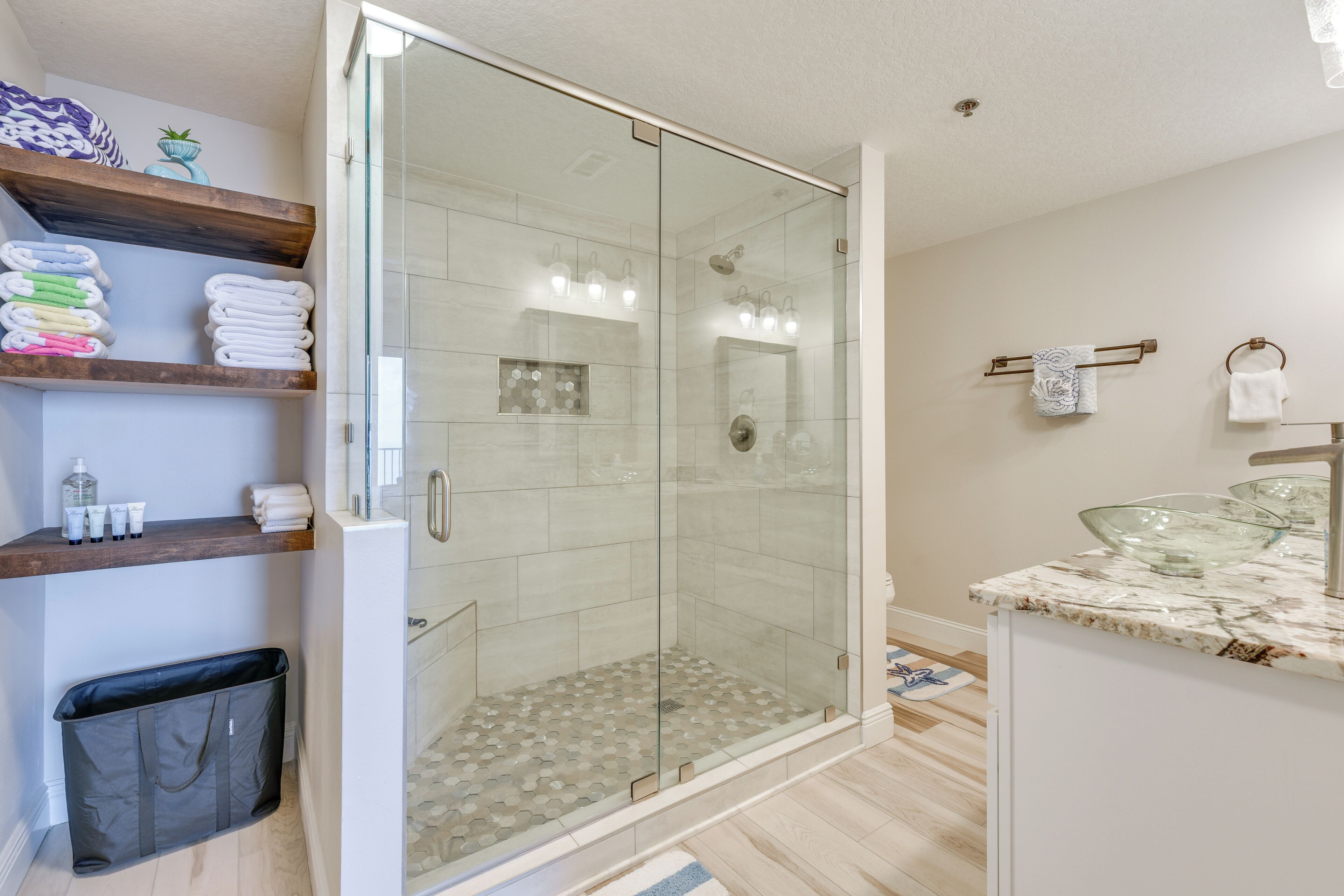 Un bagno moderno con cabina doccia in vetro, un piano di lavoro in marmo e asciugamani ordinatamente disposti su mensole.