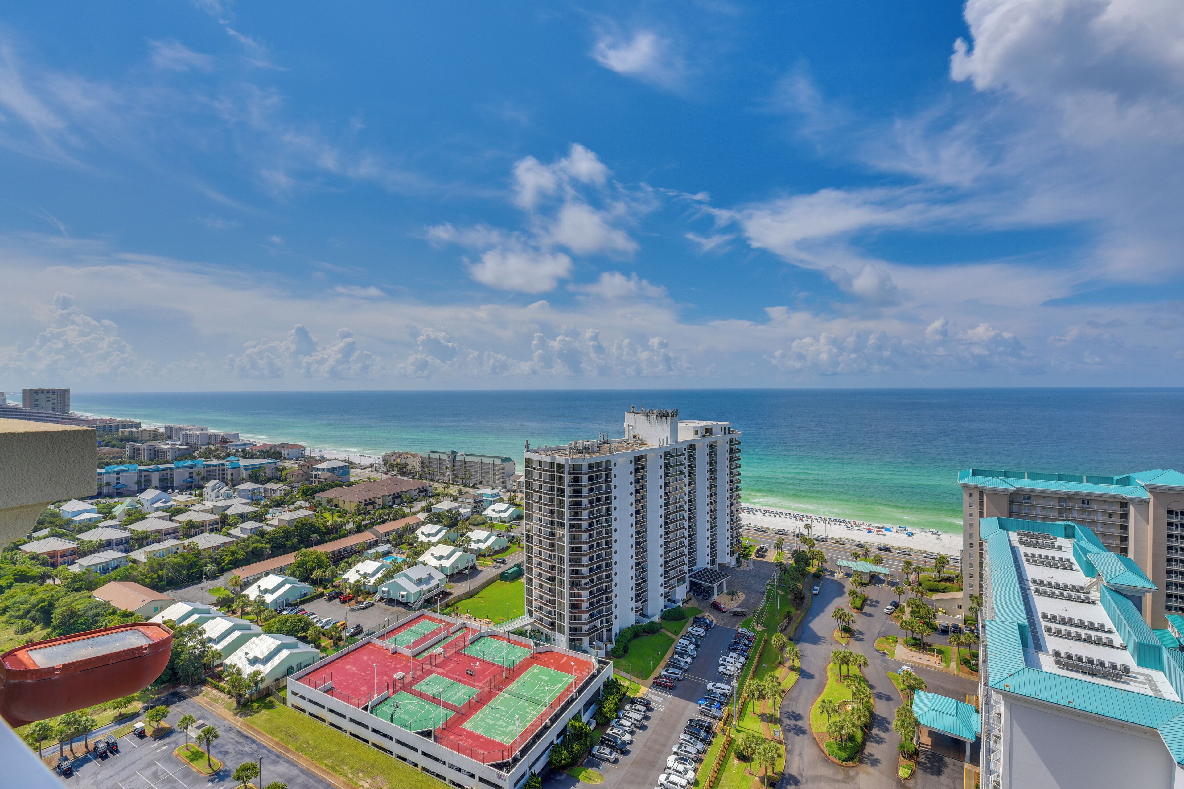 A coastal hotel with multiple buildings, a beach, and a clear sky.