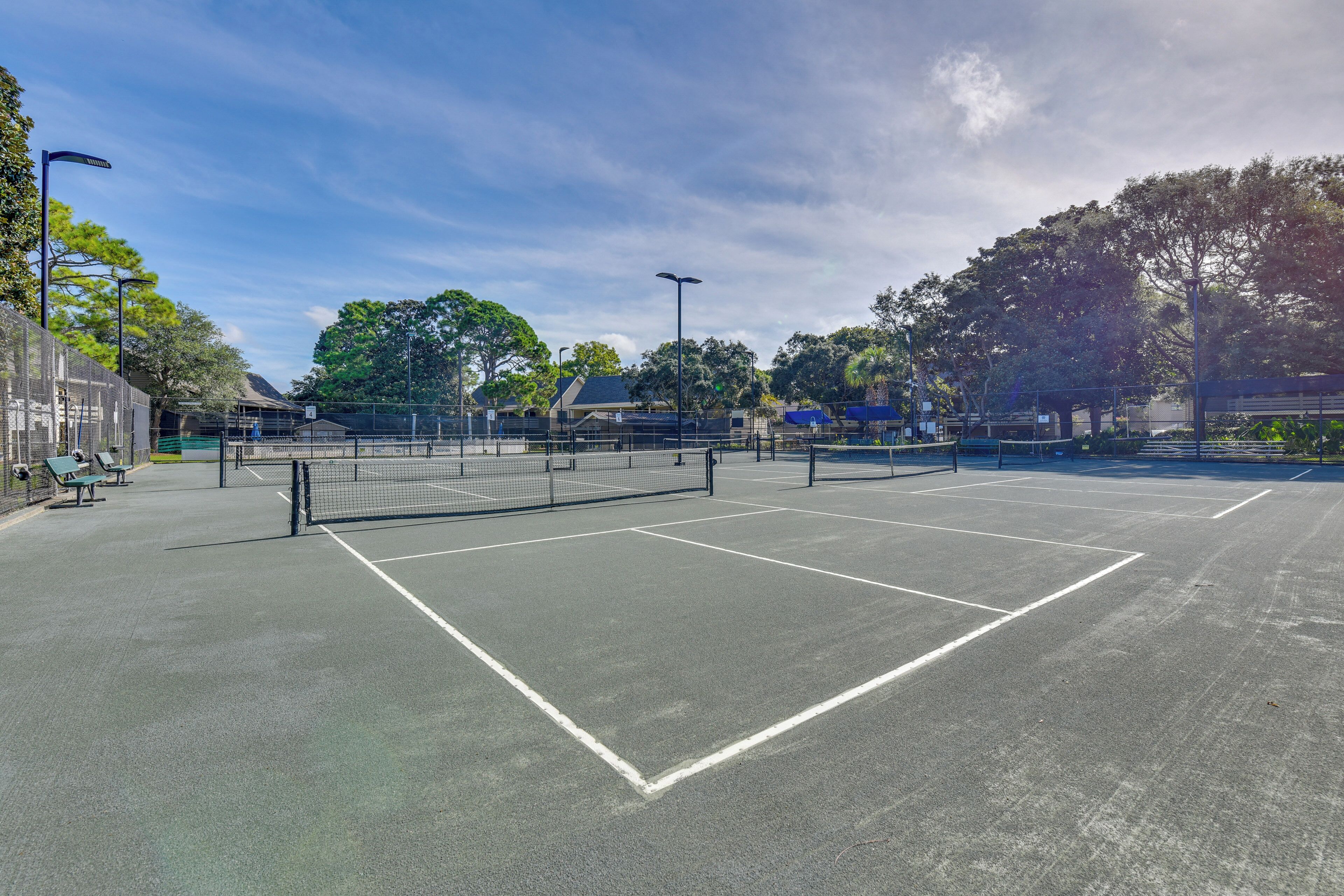 An outdoor tennis court with a net, benches, and a fence.