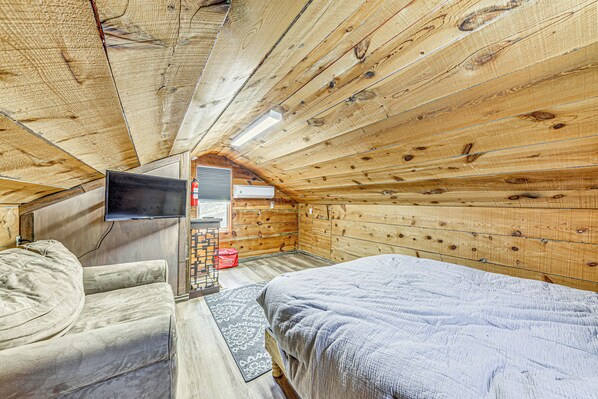 A cozy cabin room with a bed, a couch, a TV, and a small desk area. - < 1 Mi to Grindstone Lake: Cabin w/ Large Yard! (Ruidoso)