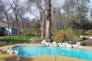 Un patio trasero con piscina, rodeado de rocas y árboles.