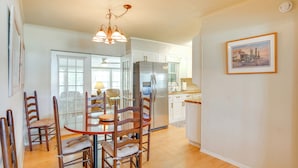 A dining area with a round table and chairs, a refrigerator, and a kitchen in the background. - Fish, Relax & Repeat: Home w/ Yard in Eastpoint! (Eastpoint)