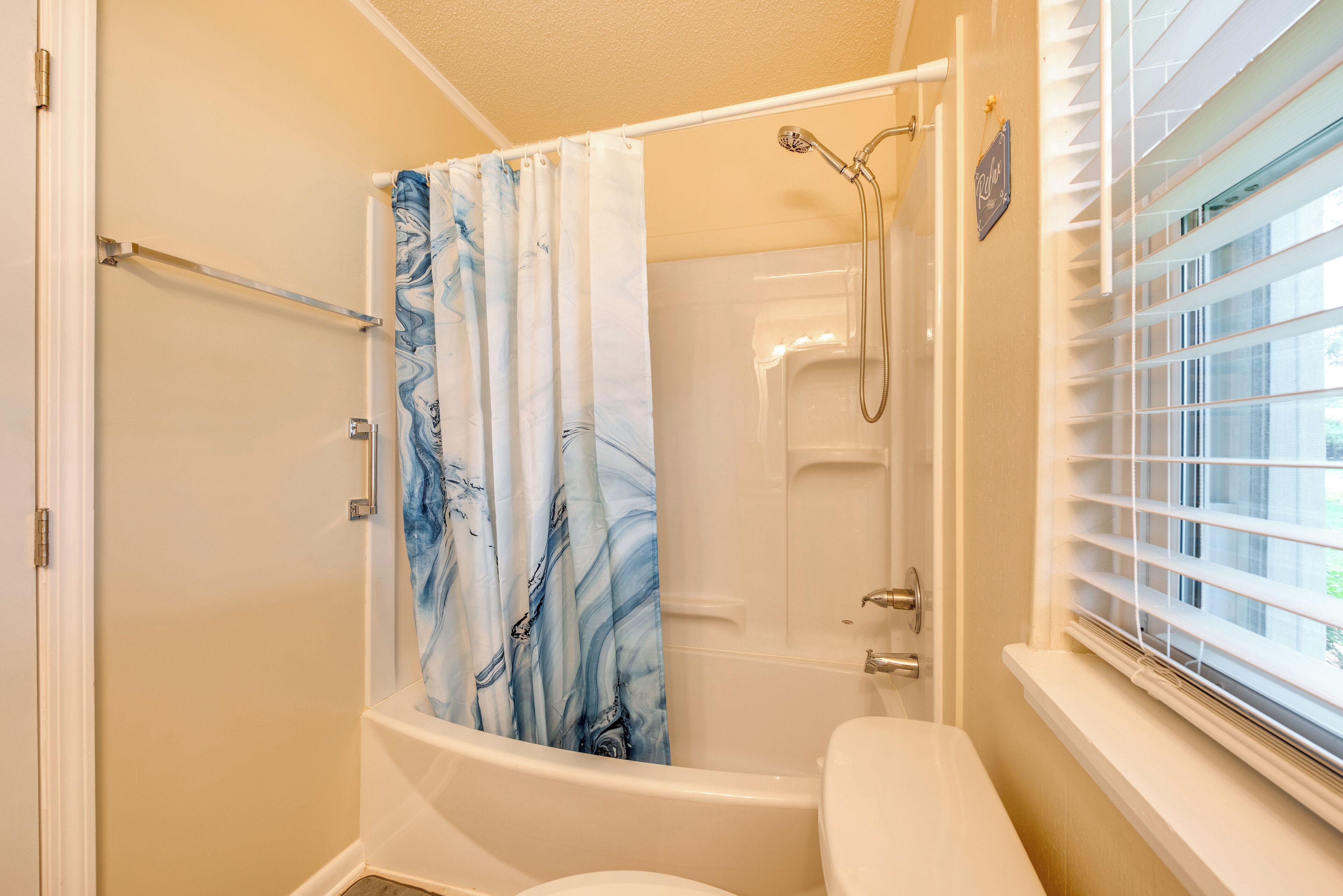 Un baño con ducha, inodoro y ventana con persianas.