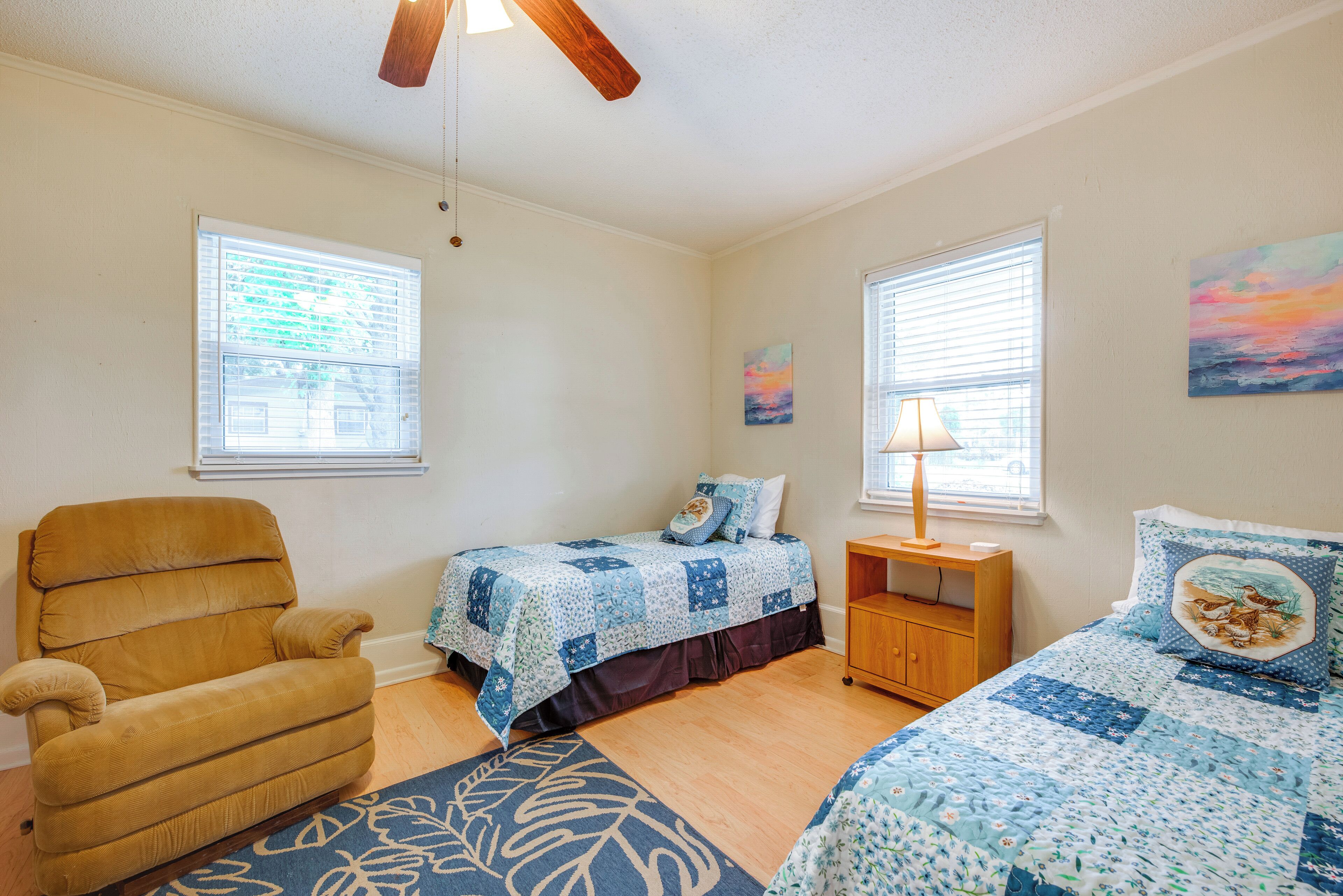 A bedroom with two beds, a wooden chair, a nightstand, and a window with blinds.