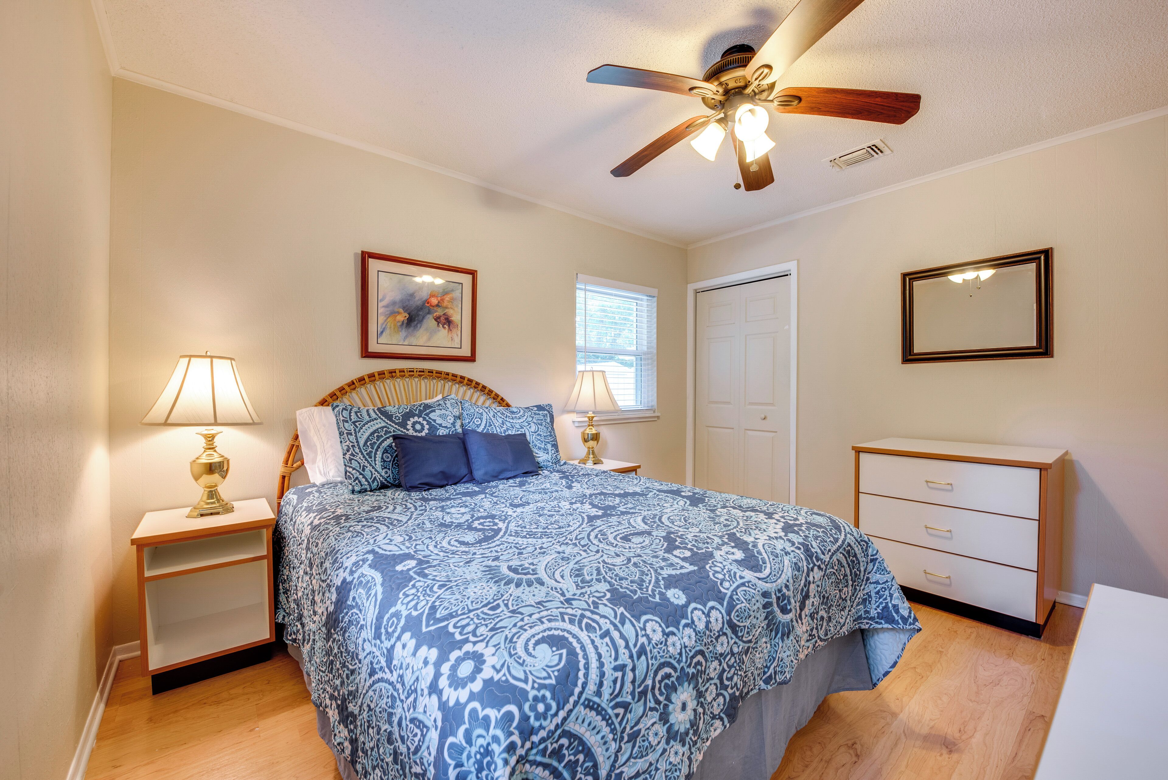 A bedroom with a bed, nightstands, a dresser, a ceiling fan, a window, and a door.