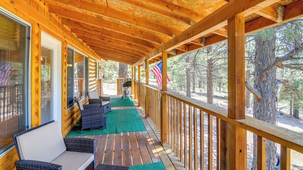 A wooden deck with wicker furniture and a green mat, overlooking a forested area. - Furnished Deck & Mountain Views: Panguitch Cabin (Panguitch)
