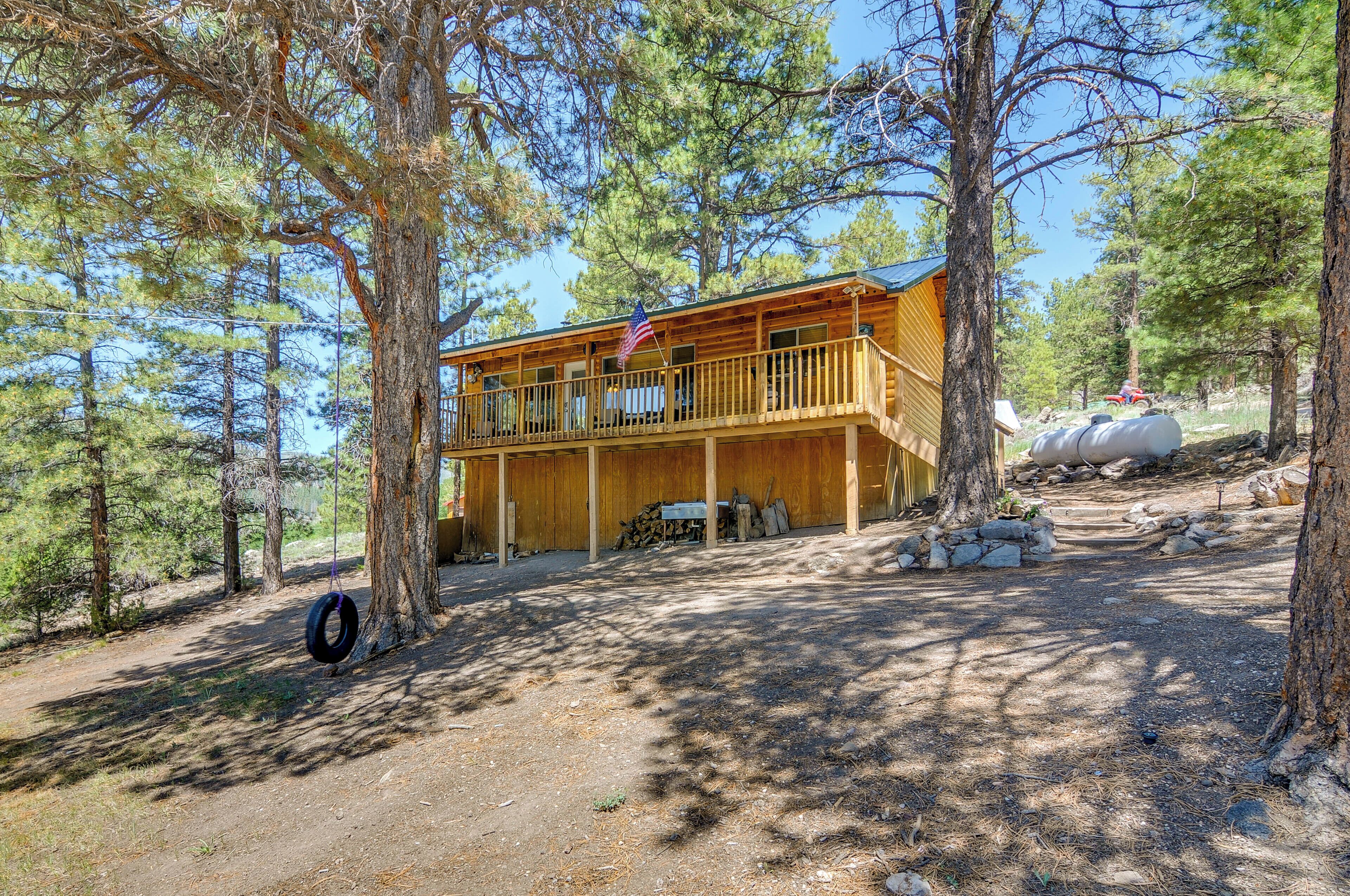 A two-story wooden cabin with a balcony, surrounded by trees and a dirt path.