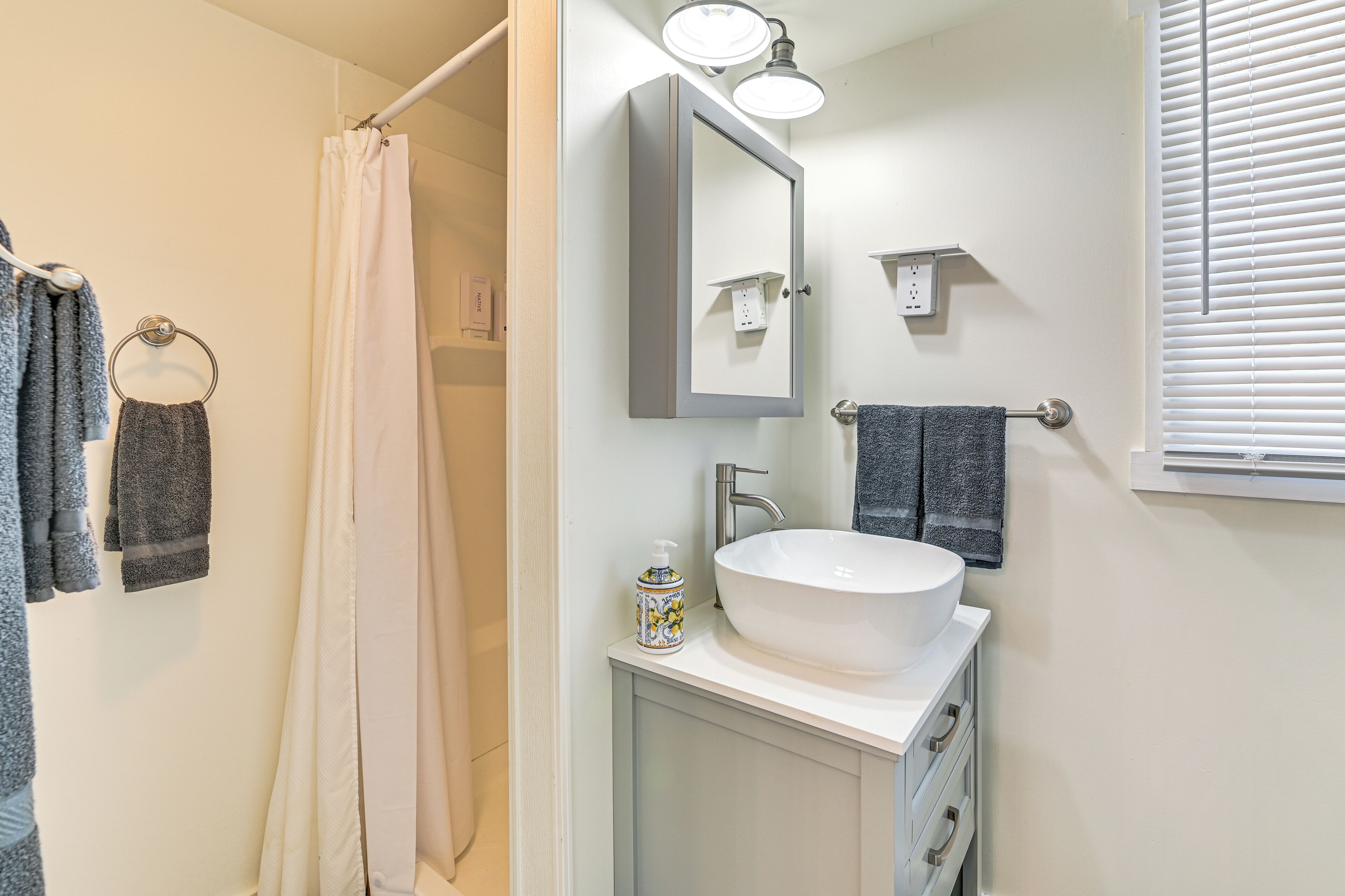Un baño con lavamanos blanco, un espejo y una cortina de ducha.