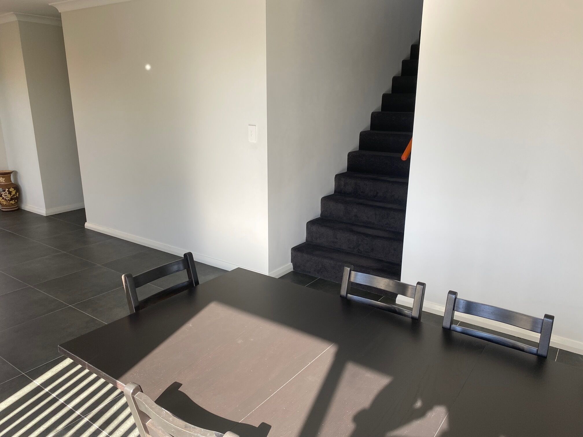 A modern interior with a dark staircase, a dining table with chairs, and a vase on the floor.