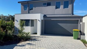 Ein modernes, zweistöckiges Haus mit Garage, befestigter Auffahrt und einer grünen Mülltonne.