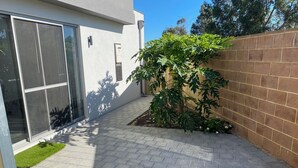Ein modernes Gebäude mit großen Glasfenstern, einem gepflasterten Innenhof und einem kleinen Garten mit einem Baum.