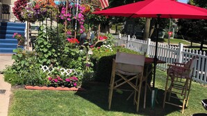 A well-maintained garden with a variety of flowers and plants, a white picket fence, and outdoor furniture. - The Abigail Manor-A night with Marilyn Monroe (Manistee)