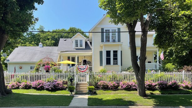 A two-story house with a white picket fence, a front porch, and a small staircase leading to the entrance. - The Abigail Manor-A night with Marilyn Monroe (Manistee)