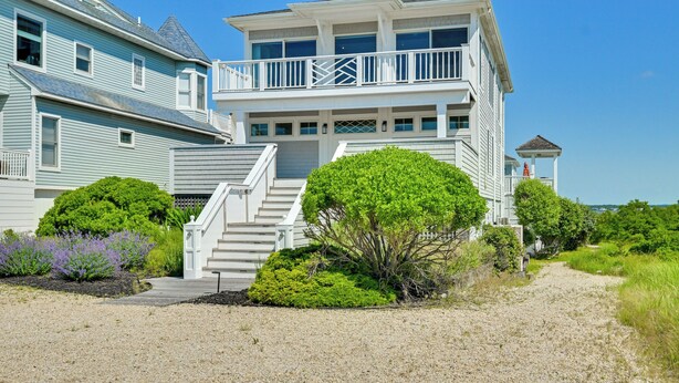 Une maison à deux étages située en bord de mer, dotée d’un balcon, d’un escalier menant à l’étage supérieur et d’une petite structure ressemblant à une tour.