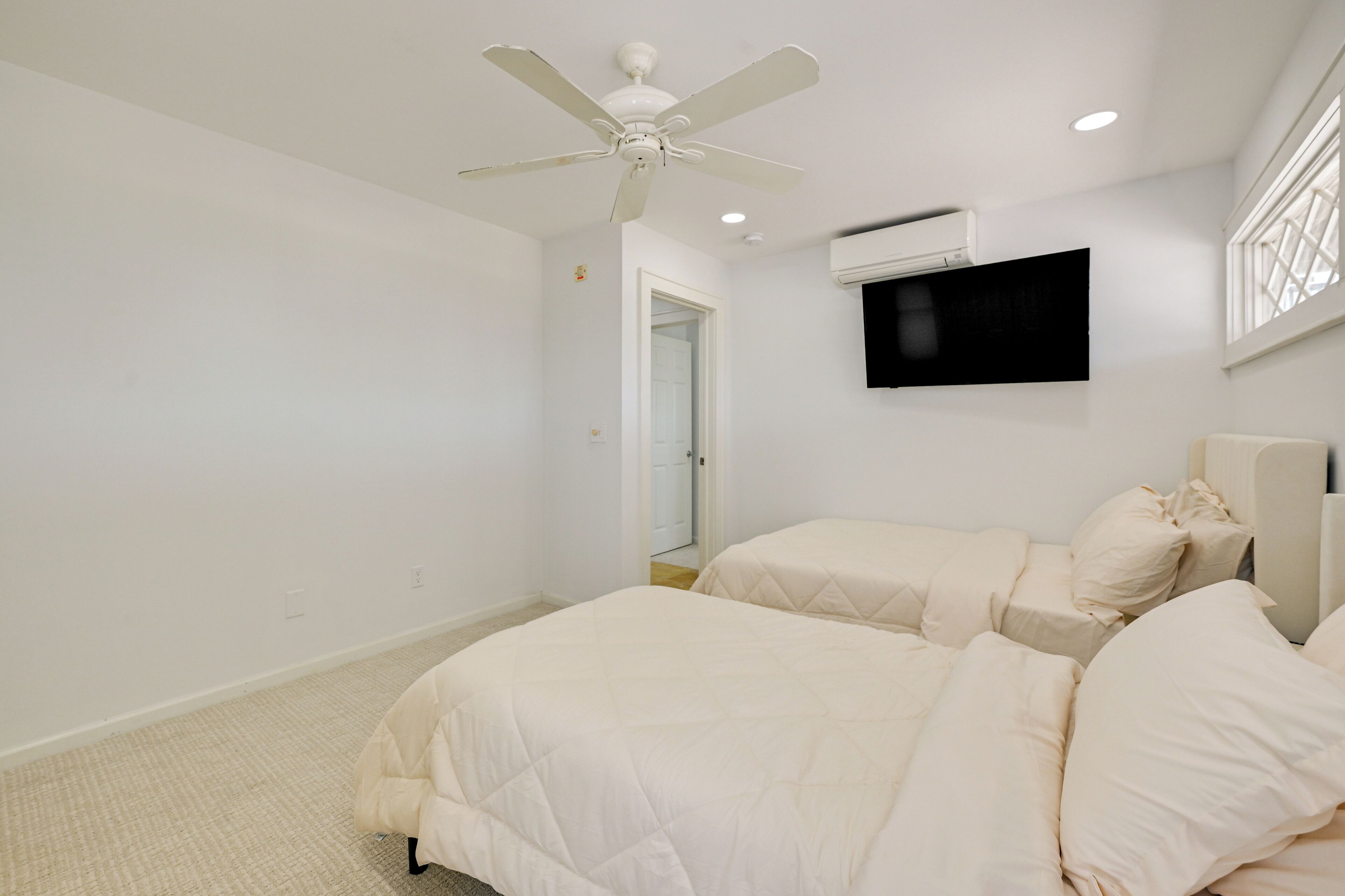 A bedroom with two beds, a ceiling fan, an air conditioning unit, and a mounted TV.