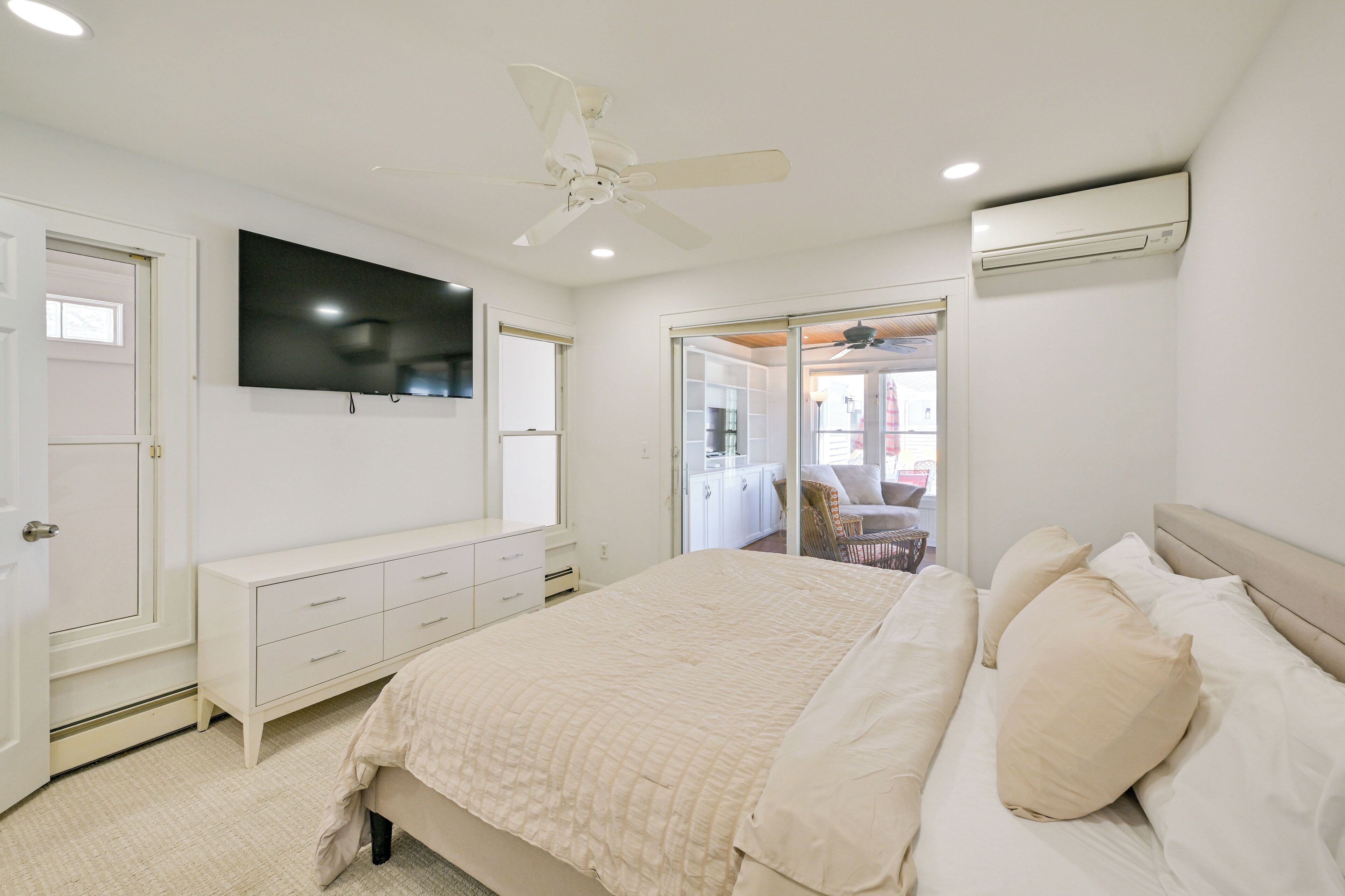 Un dormitorio con cama, televisor montado en la pared, ventilador de techo y aire acondicionado.