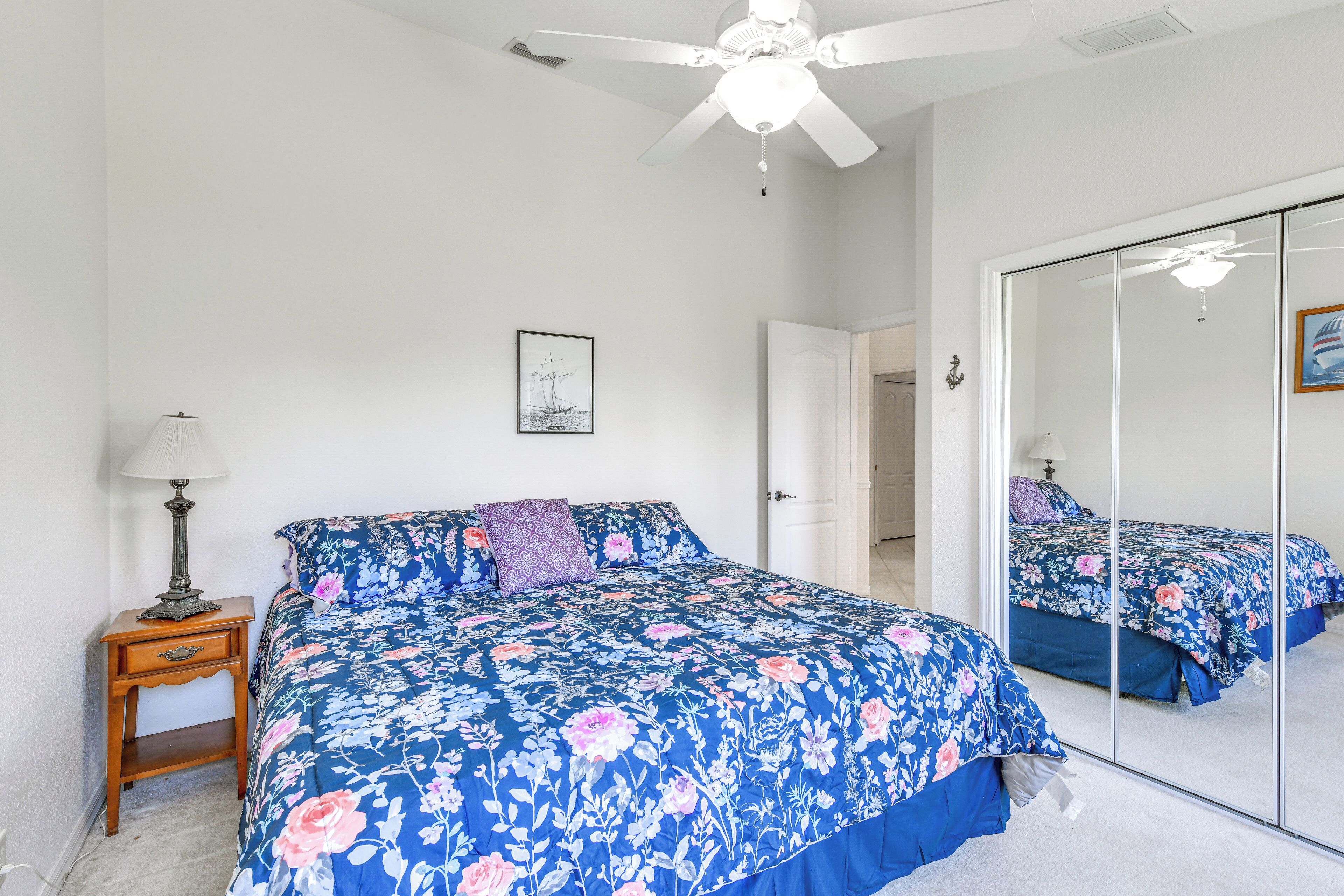 Quarto com cama, mesa de cabeceira, espelho e ventilador de teto.