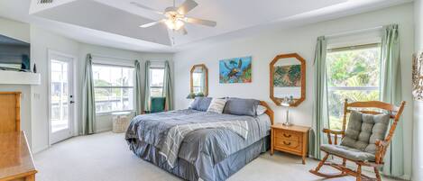 A bedroom with a large bed, a rocking chair, a ceiling fan, and artwork on the walls.