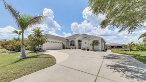 A two-story house with a driveway leading to a garage, surrounded by well-maintained lawns and palm trees. - 12 Mi to Gulf: Port Charlotte Home w/ Boat Dock (Port Charlotte)