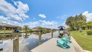 A calm waterfront area with a wooden dock, a row of turquoise chairs, and a reflection of the sky and clouds on the water. - 12 Mi to Gulf: Port Charlotte Home w/ Boat Dock (Port Charlotte)