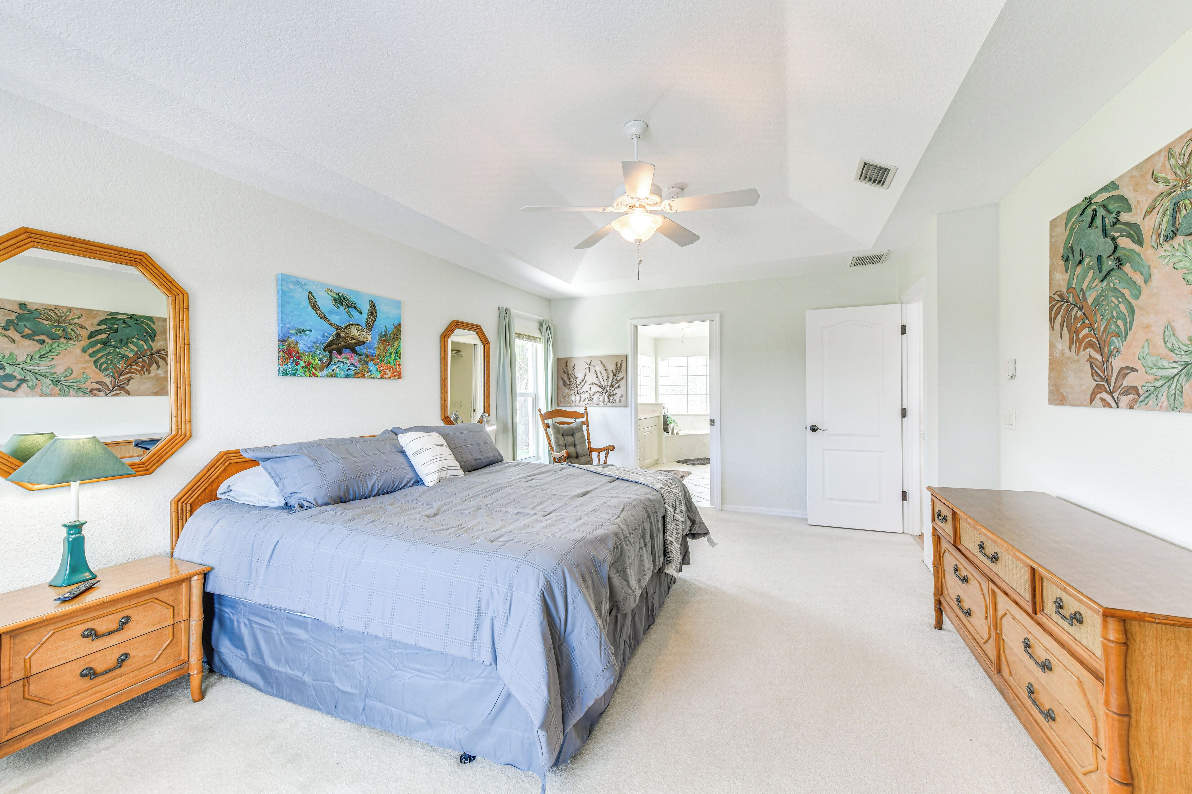 A bedroom with a bed, dresser, nightstand, ceiling fan, and artwork on the walls.