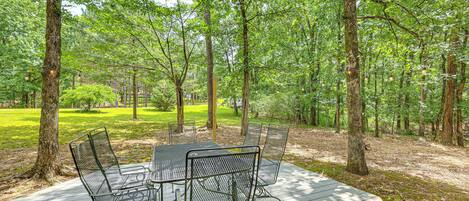 An outdoor deck with metal chairs and a table, surrounded by a forested area.