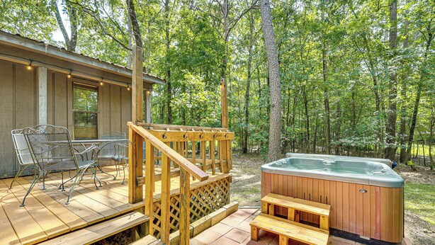 Een houten terras met buitenmeubilair, een jacuzzi en een houten trap naar een overdekt gedeelte.
