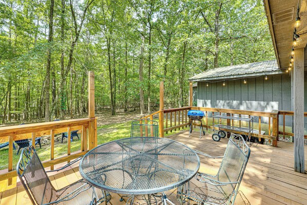 Une terrasse en bois avec une table et des chaises en métal, entourée d’arbres.
