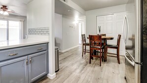 Una cucina con mobili grigi, un frigorifero in acciaio inossidabile, un tavolo da pranzo con sedie e una ventola a soffitto.