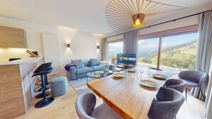 A modern living room with a dining area, a sofa set, a TV, and a large window offering a scenic view.