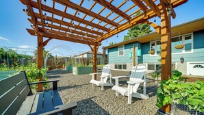 A wooden pergola with hanging lights, a bench, and white Adirondack chairs in a garden area with a house in the background. - 3 Mi to Dtwn: Family Home w/ Garden & EV Charger (Yakima)
