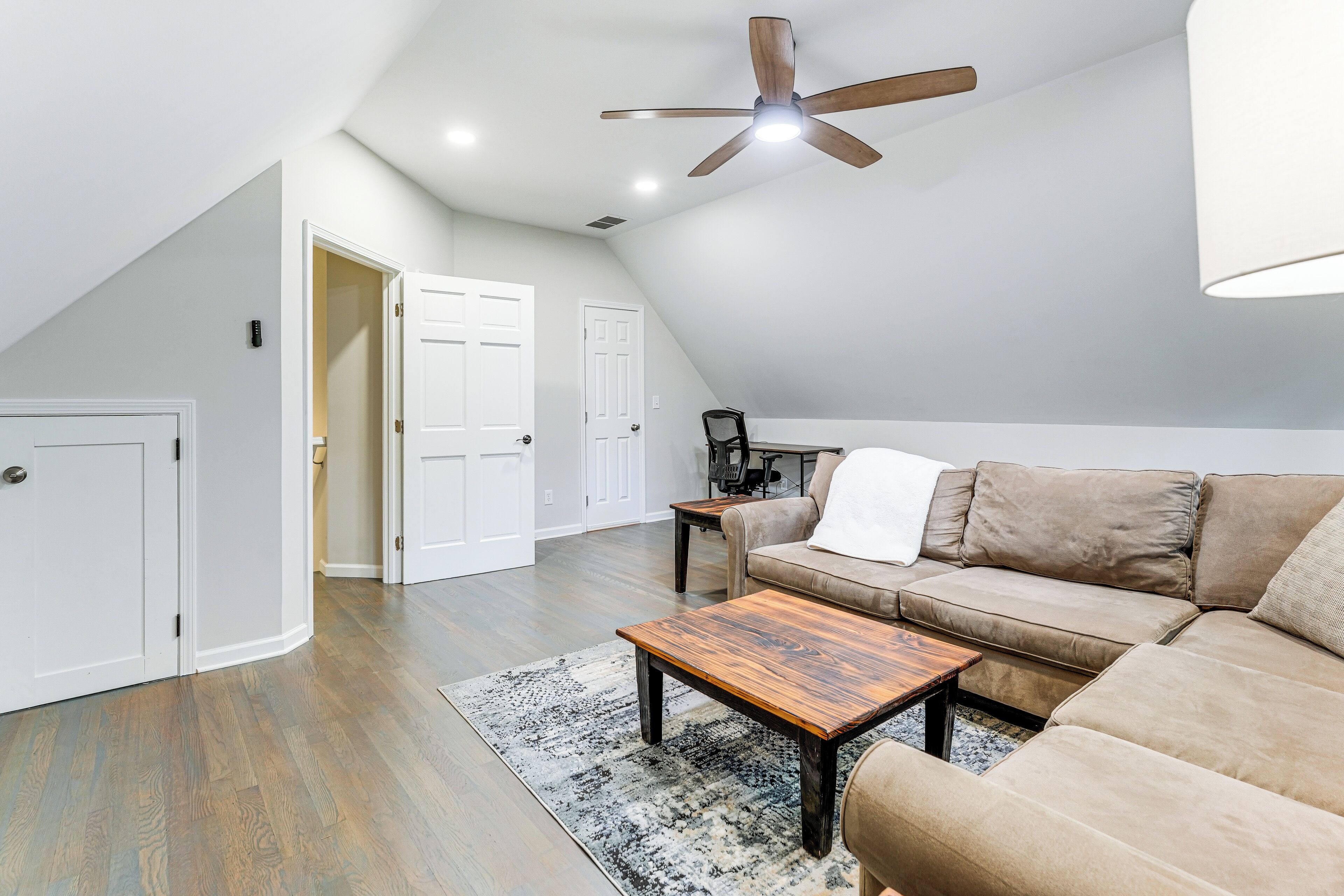 A spacious living room with a wooden coffee table, a beige sofa, and a ceiling fan.