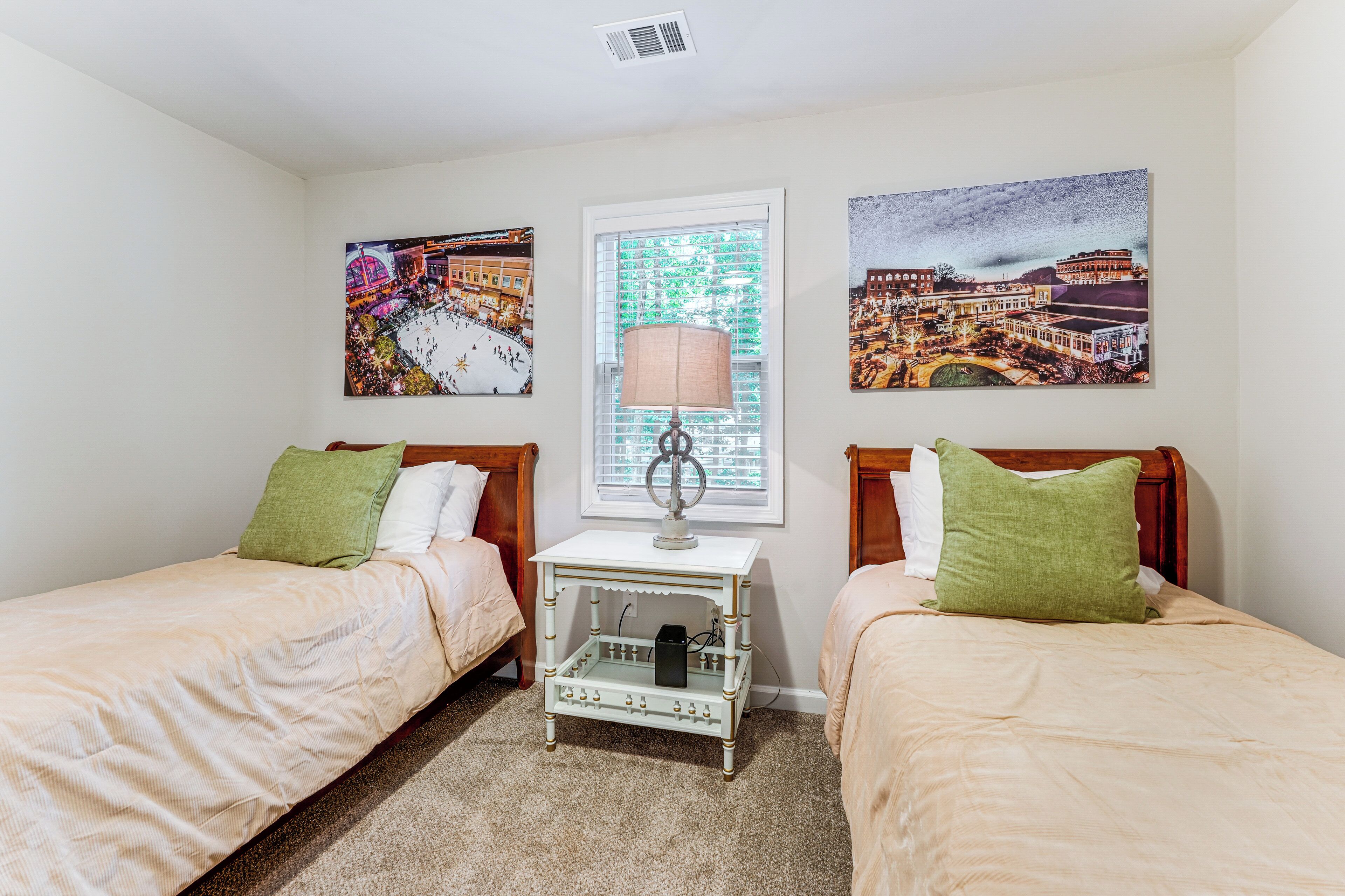 A bedroom with two beds, a nightstand, a lamp, and three wall-mounted pictures.