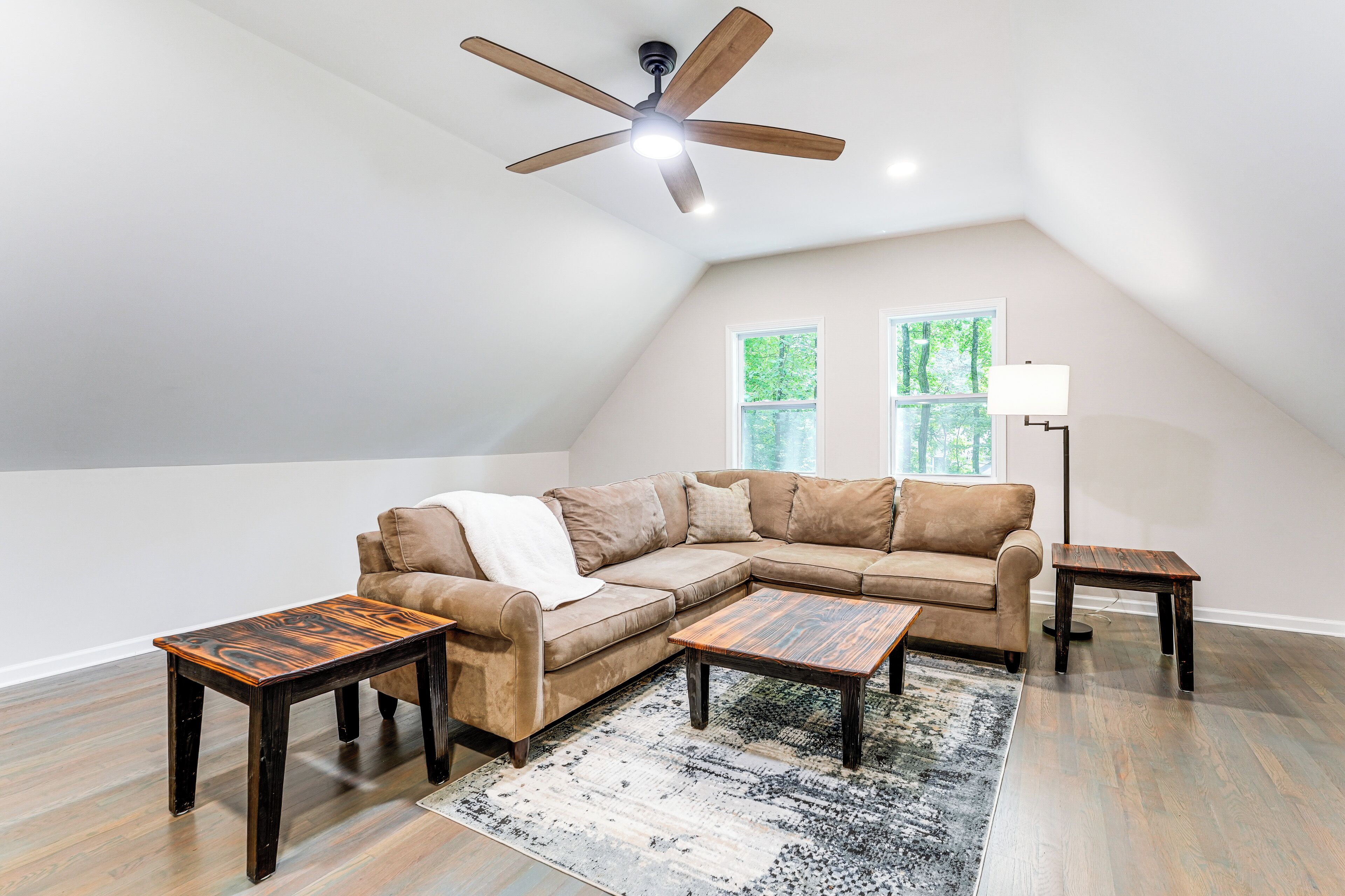 A spacious loft with a large window, a ceiling fan, and a sectional sofa.