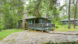 Un chalet rustique, doté d’une entrée pavée de pierres, entouré d’une forêt dense.