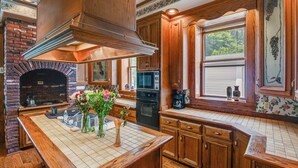 Une cuisine avec des meubles de rangement en bois, une cheminée en briques et une fenêtre donnant sur un paysage verdoyant.