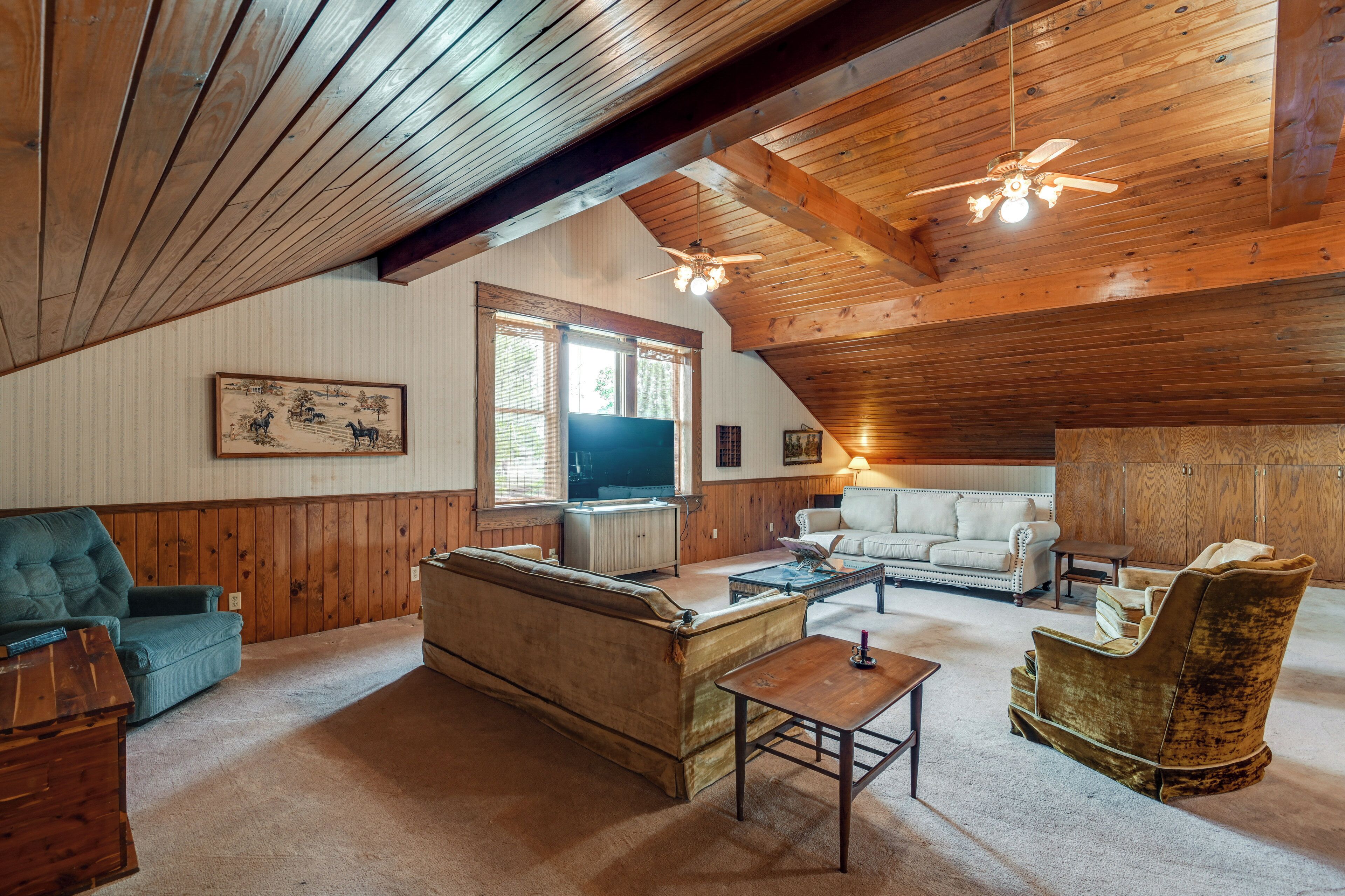 A spacious living room with wooden beams, a television, a sofa, a loveseat, a chair, and a coffee table.