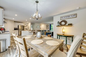 A spacious kitchen with a dining area, featuring a chandelier, a clock, and a sign that reads "The Gathering Place." - 10 Mi to Echo Lake: Wooded Escape w/ Grill! (Conway)