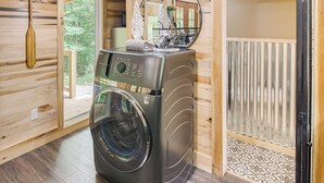 A compact, modern laundry room with a built-in washer and dryer, wooden walls, and a large mirror above the appliances. - 1 Mi to Lake: Charming Byrdstown Retreat w/ Deck! (Byrdstown)