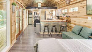 A cozy cabin interior with a kitchen, dining area, and a large bed. - 1 Mi to Lake: Charming Byrdstown Retreat w/ Deck! (Byrdstown)