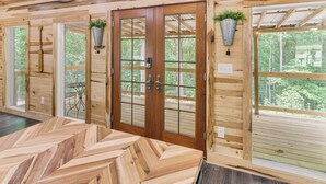 A wooden interior with large windows, a herringbone-patterned floor, and a door with a glass panel. - 1 Mi to Lake: Charming Byrdstown Retreat w/ Deck! (Byrdstown)