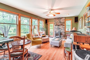 A spacious living room with large windows, a stone fireplace, and a ceiling fan. - Peaceful Country Retreat: Private & Convenient (Frenchtown)