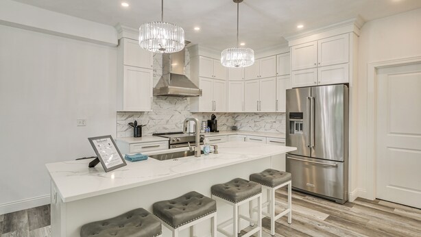 A modern kitchen with white cabinetry, a marble backsplash, stainless steel appliances, and a bar area with stools.